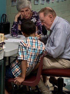 Two adults reading to an elementary school student at a table at Cornwall Manor Retirement Community